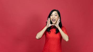 Beautiful woman wearing traditional cheongsam qipao dress calling people to wish the good luck and prosperity isolated on red background. Happy Chinese new year photo