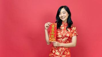 dama con traje rojo de cheongsam o qipao sosteniendo una tarjeta de bendición de la fortuna aislada en un fondo rojo. texto chino significa gran suerte gran beneficio foto