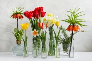 diferentes flores de primavera en jarrones transparentes sobre la mesa. tienda de flores foto
