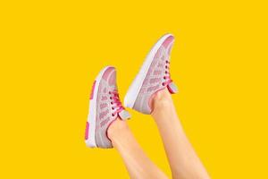 esbeltas piernas femeninas en zapatillas de deporte de moda rodadas sobre un fondo amarillo. publicidad de calzado. concepto de venta de verano. elemento de diseño foto