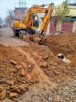 Excavator digs a large trench for pipe laying. Backhoe during earthmoving at construction site. Earth-moving heavy equipment photo