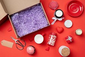 Seasonal gift box for valentine day with candle, red cup and heart shape sweets on red background photo