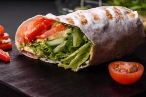 Delicious fresh shawarma with tomatoes, peppers, cucumber on a dark concrete background photo