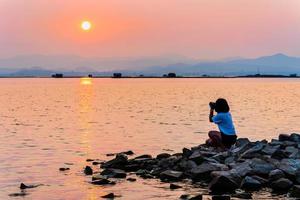 Young woman at waterfront take photos at sunset
