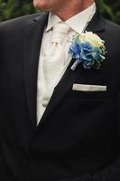 the groom in a black wedding suit, a tuxedo in a white shirt, tie and a roses buttonhole. High quality photo