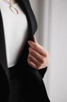 Stylish golden chain with circle on a woman's neck. Female in a black jacket and white blouse, cropped view. Elegance accessory photo