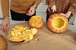 Young couple man and woman on kitchen at home making jack-o'-lantern preparing for halloween, cutting pumpkin. Cutting out faces from a fresh pumpkin. Preparing for the Halloween party celebration. photo