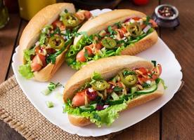 Hot dog with jalapeno peppers, tomato, cucumber and lettuce on wooden background photo