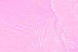 Defocus blurred transparent pink colored clear calm water surface texture with splashes and bubbles. Trendy abstract nature background. Water waves in sunlight with caustics. Pink water shinning photo