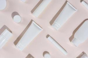 White plastic tubes, jars and other form of packaging for cosmetics on a beige background, top view. photo