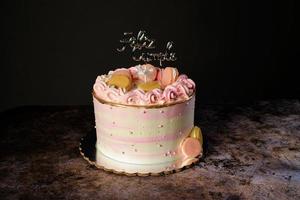 pastel de cumpleaños rosa decorado con macarons y topper de pastel con el texto feliz cumpleaños en español.