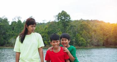 Happy family spending time outdoors hugging and enjoying the view of river. Mother with two kids. photo