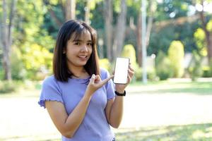 mujer asiática sonriente jugando y actualizando nuevas aplicaciones su mano señaló el teléfono con el área de trabajo de la pantalla en blanco charlando. enfoque suave y selectivo. foto