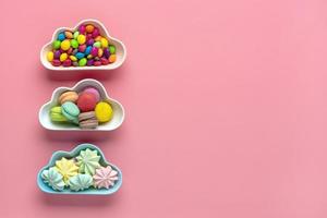 caramelos coloridos - piruletas, merengues, macarrones en un tazón en forma de nube aislado sobre fondo rosa vista plana endecha superior knolling comida poco saludable y sabrosa concepto creativo tarjeta de vacaciones foto