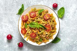 fusilli - pasta italiana clásica de trigo duro con carne de pollo, tomates cherry, albahaca en salsa de tomate en un tazón blanco sobre una mesa de hormigón gris cocina mediterránea vista superior plana foto