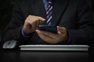 Business man holding mobile smartphone and keyboard computer on desk. photo