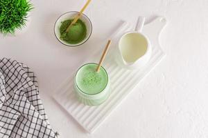 tea ceremony. matcha latte green tea with milk in a glass on a white ceramic board, a jug of milk, a bowl of green powder. an alternative to coffee. photo