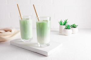 Matcha latte tea in tall glasses with straw on a white wooden board. a healthy drink. purification of the body, improvement of metabolism. photo