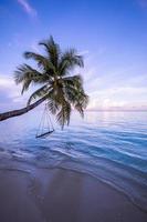 A view of a beach with palm trees and swing at sunset. Unique landscape, serene peaceful paradise. Perfect romantic beach sunset scenery, calm sea, colorful sky. Beautiful tropical nature pattern