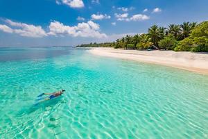 Caucasian couple of tourists snorkel in crystal turquoise water near Maldives Island. Perfect weather conditions at luxury resort beach scene, calm sea water, couple exotic water, underwater wildlife photo