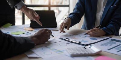 gente de negocios reunida usando computadora portátil, calculadora, cuaderno, papel gráfico del mercado de valores para planes de análisis para mejorar la calidad el próximo mes. conferencia discusión concepto corporativo foto