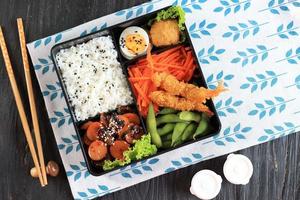 vista superior caja bento japonesa con salchicha teriyaki, zanahoria, huevo al vapor, nugget y camarones tempura foto