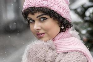 Portrait of a smiling stylish young woman in pastel-colored warm clothes outdoors in the city in winter.Snowfall,cold weather photo