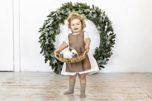 una niña sostiene una canasta con un conejo en el fondo de las decoraciones navideñas. símbolo del nuevo año 2023. foto