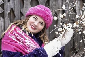 retrato de una joven sonriente con una bufanda y un sombrero de color rosa brillante, mitones blancos y un abrigo de piel púrpura al aire libre en un parque de la ciudad en invierno. foto