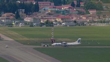 SOCHI, RUSSIA JULY 27, 2022 - Tractor towing turboprop aircraft of UTair at Sochi International Airport. Tourism and travel concept. Long shot, airplane on the airfield video