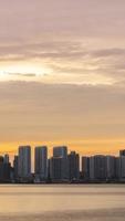 verticaal timelapse silhouet visie van waterkant stad met hoogbouw wolkenkrabber gebouw in de buurt zee kust strand terwijl zonsondergang zonsondergang tijd met vanille schemering lucht video