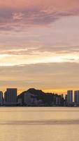 timelapse vertical silhouette vue de la ville au bord de l'eau avec un gratte-ciel de grande hauteur près de la plage de la côte de la mer pendant le coucher du soleil au coucher du soleil avec un ciel crépusculaire à la vanille video
