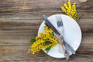 Fork knife with plate and mimosa flowers on wooden table for spring Easter holiday dinner. photo