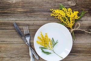 Fork knife with plate and mimosa flowers on wooden table for spring Easter holiday dinner. photo