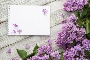 Clean notepad with spring lilac flowers on white wooden background photo