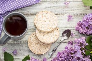 Cup of tea with crispbreads decorated spring lilac flowers on white wooden background photo