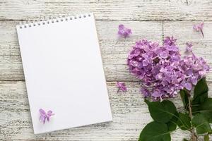 Clean notepad with spring lilac flowers on white wooden background photo