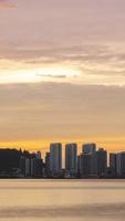 vista de silhueta de timelapse vertical da cidade à beira-mar com arranha-céus arranha-céus perto da praia da costa do mar enquanto o pôr do sol ao pôr do sol com céu crepúsculo de baunilha video