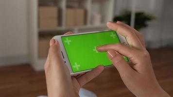 Closeup horizontal of hand woman holding smartphone with green screen while sitting in living room. Blank digital smartphone in hand girl. Showing content videos blogs on center screen.