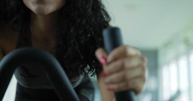 Handheld panning slow motion shot, Asian young female holding on handle while spinning on stationary bike in gym for workout video