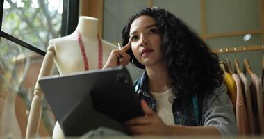 prise de vue à la main, une jeune créatrice de mode réfléchie se fait une idée et utilise un croquis au stylo numérique dessinant sur une tablette dans un studio de vêtements de mode, une petite entreprise et un concept d'entrepreneuriat. video