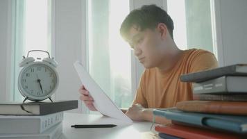 homem estudante asiático tem ansiedade por causa dos exames, o homem se prepara para o teste e aprende lições na biblioteca. estresse, desespero, pressa, leitura mal-entendida, desencorajado, expectativa, conhecimento, cansado video