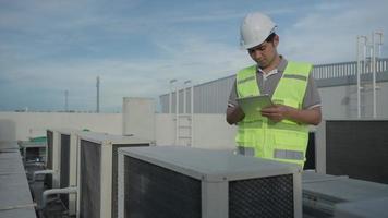 ingeniero de mantenimiento asiático trabaja en el techo de la fábrica. el contratista inspecciona el sistema de compresores y planifica la instalación de sistemas de aire acondicionado en la construcción. tecnología, verificación en línea, aplicación móvil. video