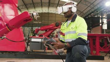 ein afroamerikanischer ingenieur mit vr-brille steuert roboterarm, virtuelle simulatorsoftware in der mechanischen fertigungsfabrik und intelligente automatische maschinentechnologie in der brancheninnovation. video