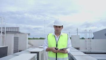 Asian maintenance engineer works on the roof of factory. contractor inspect compressor system and plans installation of air condition systems in construction. technology, online checking, mobile video