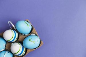 top view easter colorful handmade painted blue eggs in a box on purple background photo