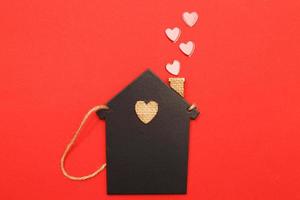 pequeña casa de juguete con corazones rojos de tubería sobre fondo rojo. concepto de amor, familia foto