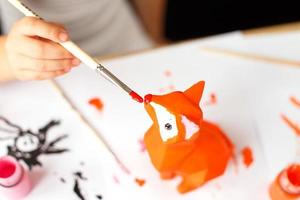 a little girl paints a toy fox made of clay. DIY concept photo