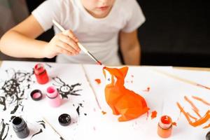 una niña pequeña pinta un zorro de juguete hecho de arcilla. concepto de bricolaje foto