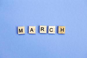 inscription March made by wooden cubes on a veri peri purple background. photo